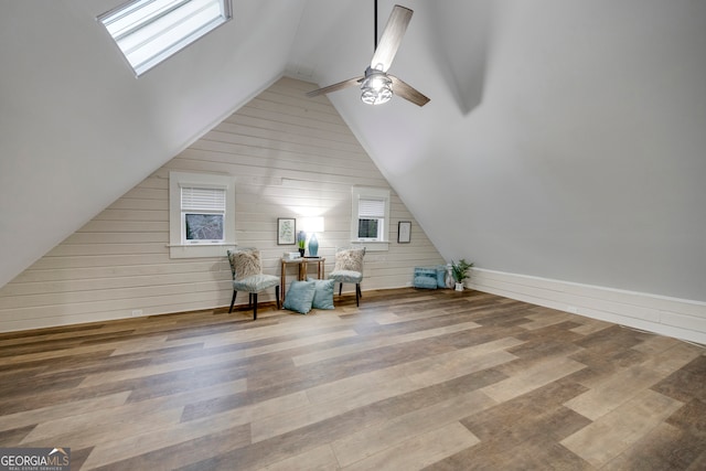 unfurnished room with hardwood / wood-style floors, ceiling fan, wooden walls, and vaulted ceiling with skylight