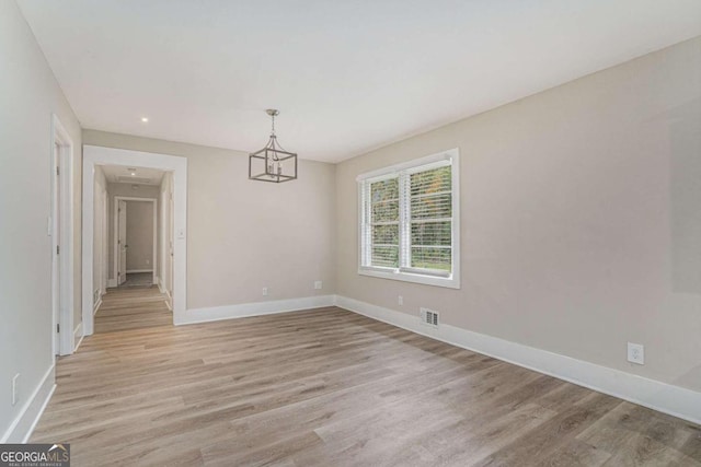 empty room featuring an inviting chandelier and light hardwood / wood-style flooring