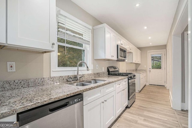 kitchen featuring sink, light hardwood / wood-style flooring, light stone countertops, white cabinetry, and stainless steel appliances