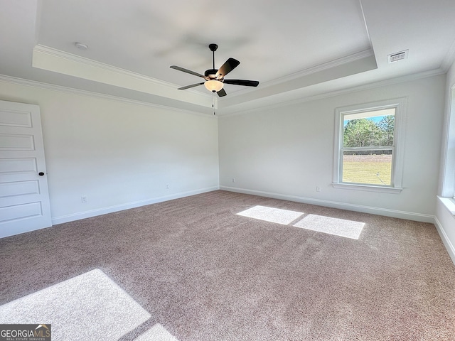 empty room with a raised ceiling, crown molding, and carpet floors