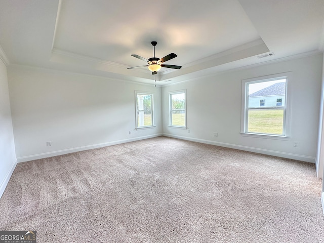 empty room with ceiling fan, a raised ceiling, carpet floors, and ornamental molding