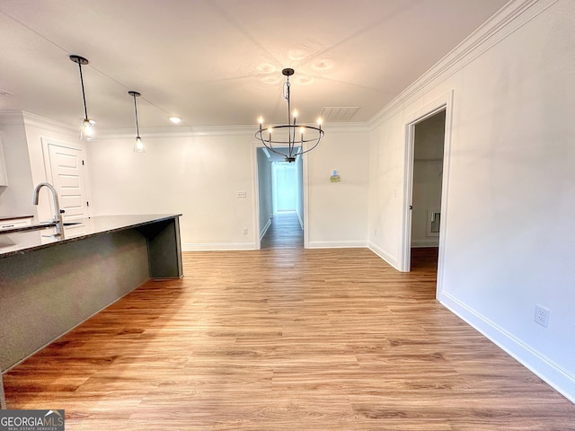 unfurnished dining area featuring light hardwood / wood-style floors, crown molding, sink, and an inviting chandelier