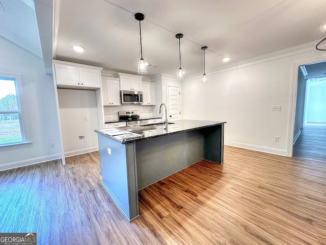 kitchen with dark stone counters, white cabinets, an island with sink, appliances with stainless steel finishes, and decorative light fixtures