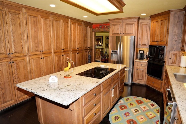 kitchen featuring black appliances, dark hardwood / wood-style floors, a kitchen island, and light stone counters