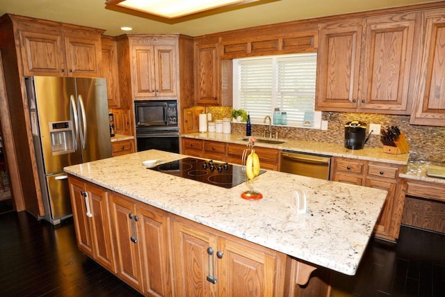 kitchen with sink, a center island, light stone counters, dark hardwood / wood-style floors, and black appliances