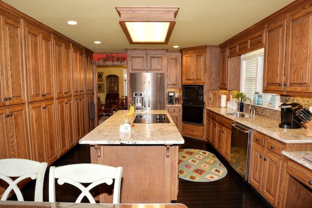 kitchen with sink, light stone counters, a breakfast bar, a kitchen island, and black appliances