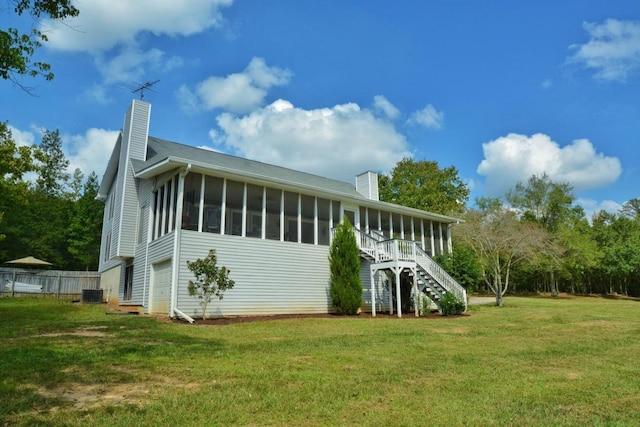 rear view of house with a sunroom, a garage, central air condition unit, and a lawn