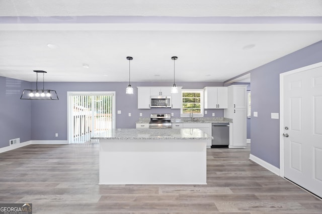 kitchen with sink, white cabinets, pendant lighting, a kitchen island, and appliances with stainless steel finishes