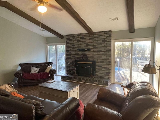 living room with a wood stove, ceiling fan, vaulted ceiling with beams, hardwood / wood-style floors, and a textured ceiling