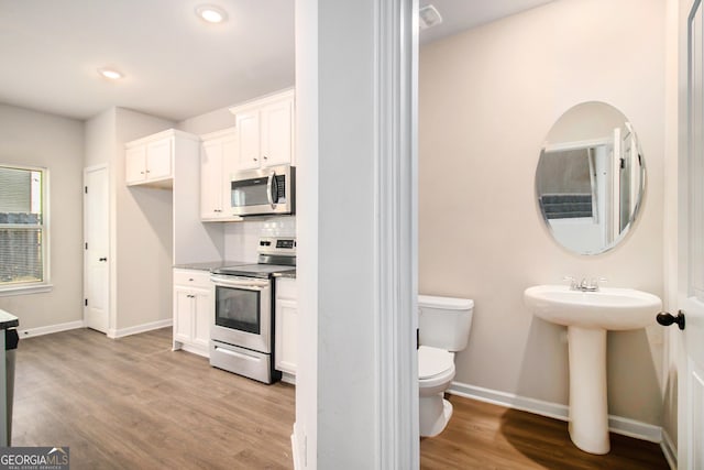 kitchen with white cabinets, backsplash, stainless steel appliances, and light hardwood / wood-style floors