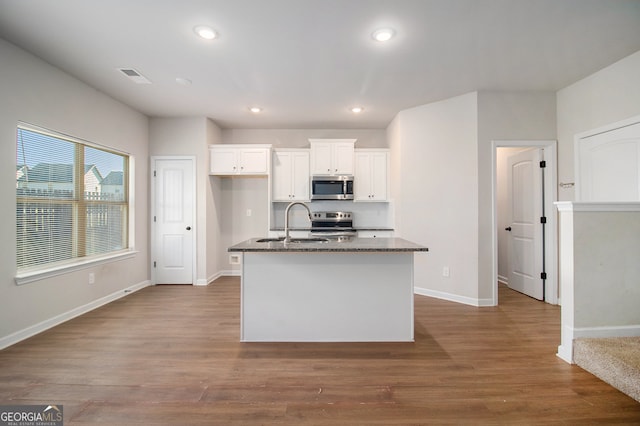 kitchen with stainless steel appliances, white cabinetry, hardwood / wood-style flooring, and dark stone counters