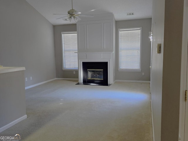 unfurnished living room with plenty of natural light, light colored carpet, ceiling fan, and a large fireplace