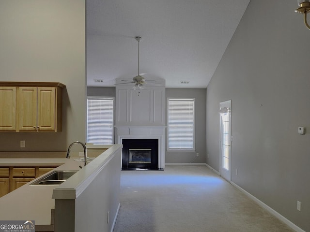 kitchen with light carpet, light brown cabinetry, sink, a large fireplace, and lofted ceiling