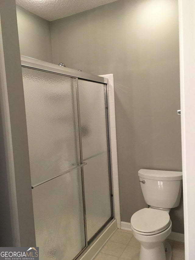 bathroom featuring a textured ceiling, toilet, walk in shower, and tile patterned flooring