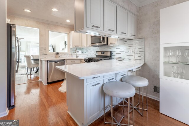 111 Swanton Hill Ct, Decatur, GA 30030 - kitchen featuring light wood-type flooring, stainless steel appliances, a peninsula, crown molding, and light countertops