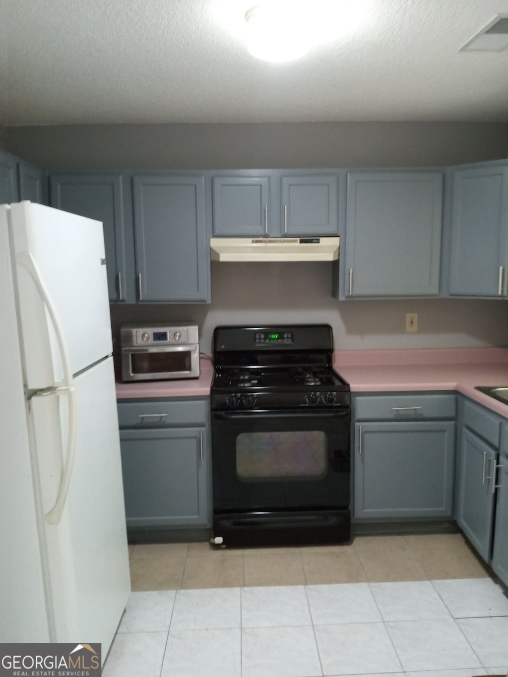 kitchen with black gas stove, light tile patterned floors, a textured ceiling, and white refrigerator