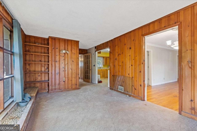 unfurnished living room featuring light colored carpet, an inviting chandelier, ornamental molding, and wood walls