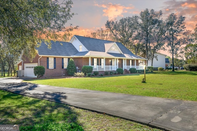 cape cod home featuring a garage, covered porch, and a yard