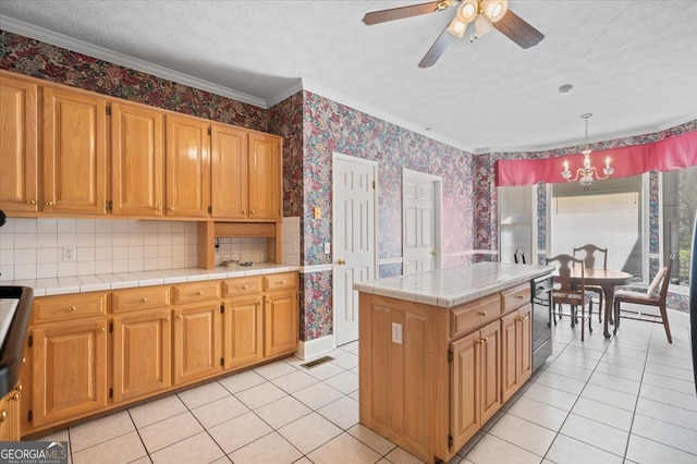 kitchen featuring tile countertops, crown molding, pendant lighting, a textured ceiling, and ceiling fan with notable chandelier