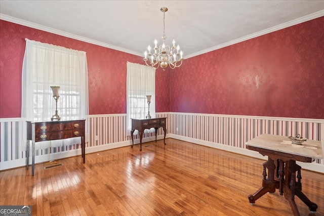 dining area with wood-type flooring, ornamental molding, and a notable chandelier