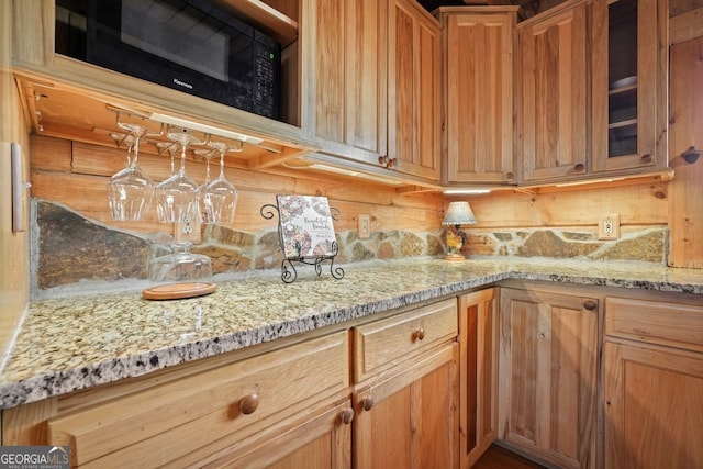 kitchen with glass insert cabinets, black microwave, brown cabinetry, and light stone counters