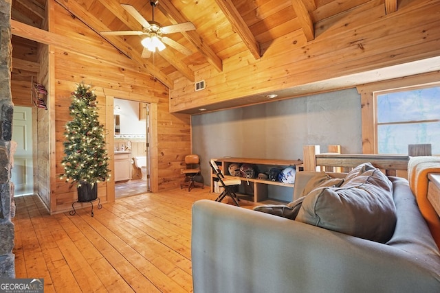 living room featuring ceiling fan, beamed ceiling, light hardwood / wood-style floors, wooden walls, and wood ceiling