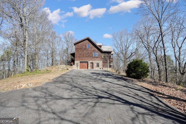 view of side of home featuring aphalt driveway, stone siding, and a garage