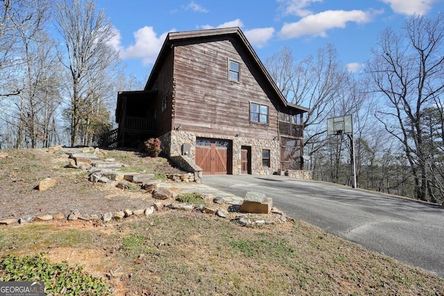 view of side of property with aphalt driveway, stone siding, and an attached garage