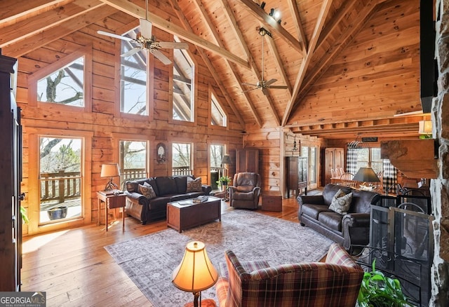 living room with beam ceiling, light wood-style flooring, wood ceiling, wood walls, and ceiling fan