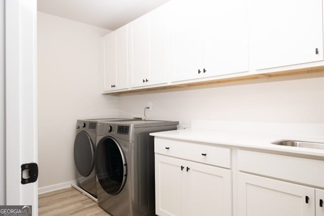 laundry area featuring cabinets, washing machine and dryer, and light hardwood / wood-style flooring