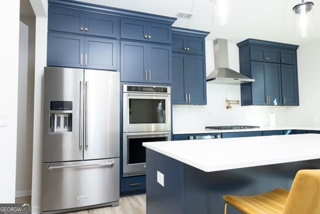 kitchen with a breakfast bar, stainless steel appliances, blue cabinetry, and wall chimney exhaust hood