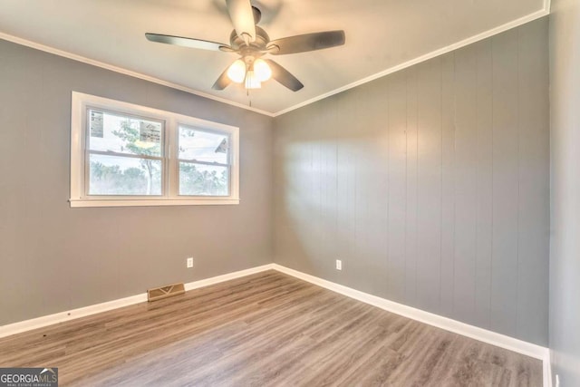 empty room with hardwood / wood-style floors, wooden walls, ceiling fan, and ornamental molding