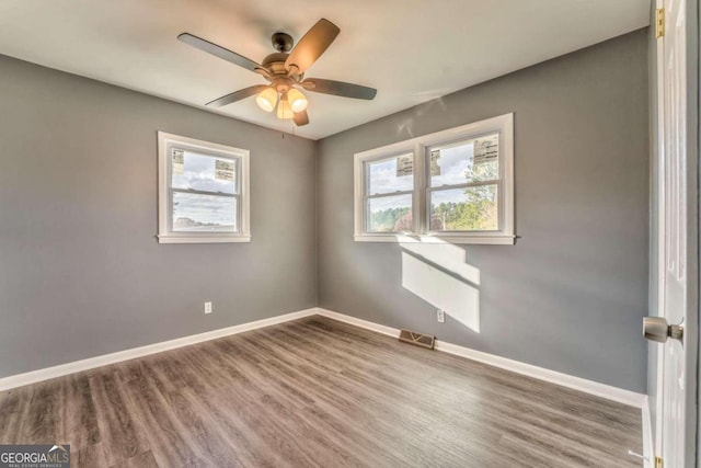 empty room with ceiling fan, plenty of natural light, and wood-type flooring