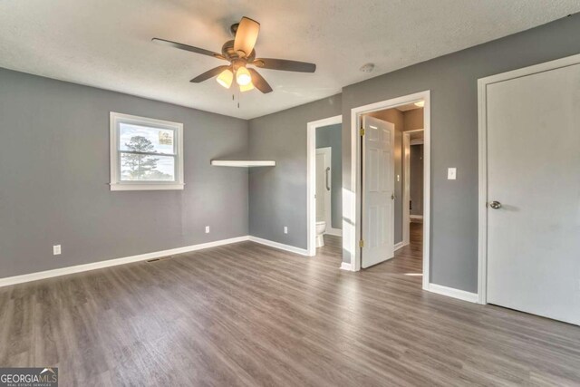 unfurnished bedroom with ceiling fan, wood-type flooring, a textured ceiling, and ensuite bath