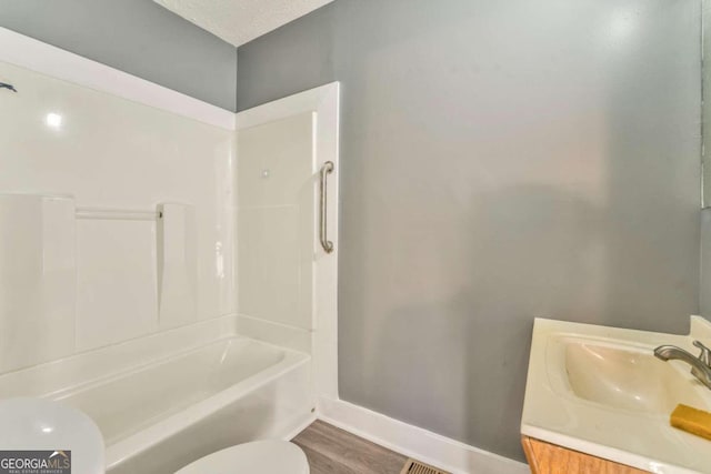 full bathroom featuring washtub / shower combination, wood-type flooring, a textured ceiling, toilet, and vanity