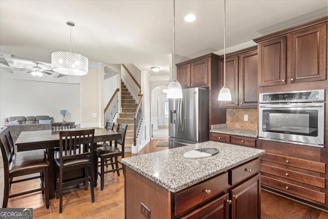 kitchen featuring appliances with stainless steel finishes, tasteful backsplash, decorative light fixtures, light hardwood / wood-style floors, and a kitchen island