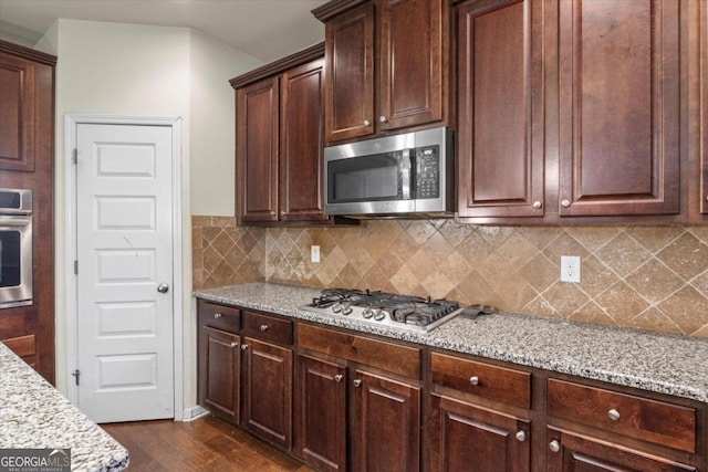 kitchen featuring dark hardwood / wood-style flooring, light stone countertops, backsplash, and appliances with stainless steel finishes