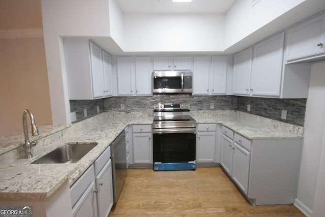 kitchen featuring kitchen peninsula, appliances with stainless steel finishes, light stone counters, sink, and light hardwood / wood-style floors