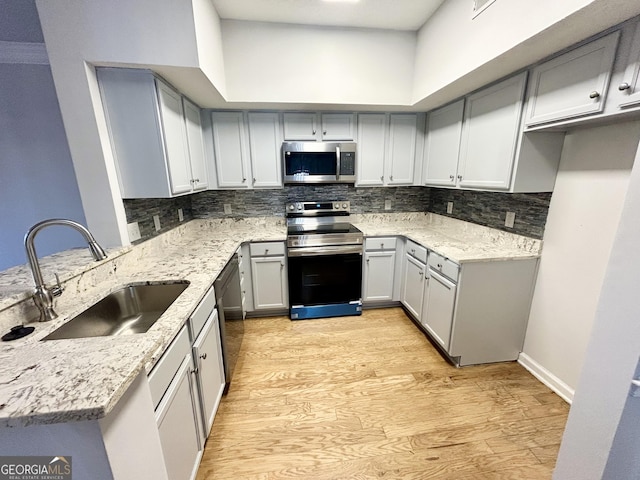 kitchen with light stone counters, sink, stainless steel appliances, and light hardwood / wood-style floors