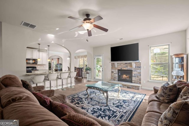 living room with carpet, a stone fireplace, and ceiling fan