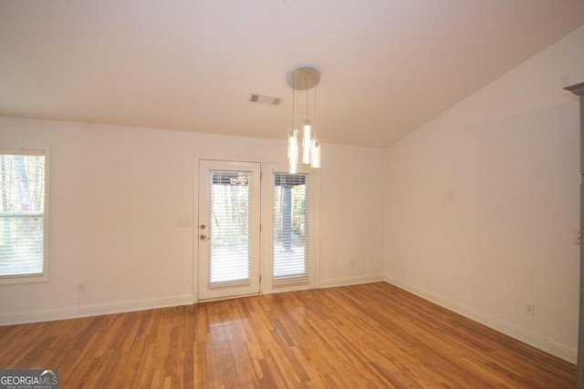 spare room with wood-type flooring, an inviting chandelier, and vaulted ceiling