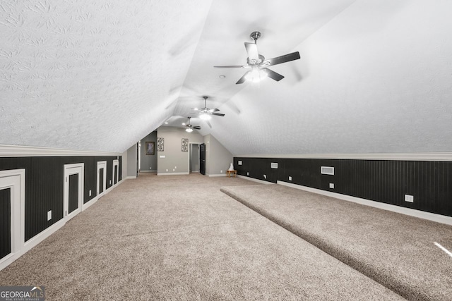 additional living space with carpet, a textured ceiling, vaulted ceiling, and ceiling fan