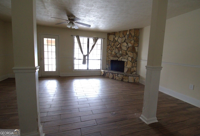 unfurnished living room with ceiling fan, a stone fireplace, a textured ceiling, and dark wood-type flooring