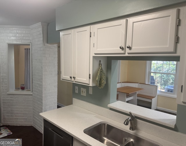 kitchen with brick wall, crown molding, sink, dishwasher, and white cabinets