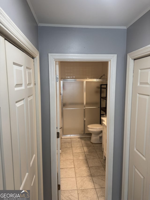 bathroom with tile patterned floors, crown molding, a shower with door, and toilet