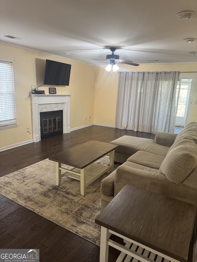 living room featuring a high end fireplace, ornamental molding, ceiling fan, and dark wood-type flooring