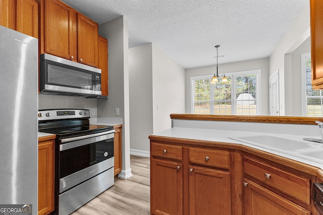 kitchen with sink, hanging light fixtures, light wood-type flooring, a notable chandelier, and stainless steel appliances