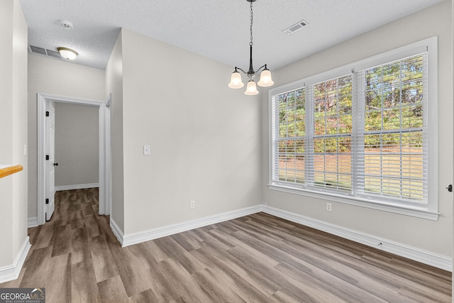 spare room with wood-type flooring, a textured ceiling, and a notable chandelier