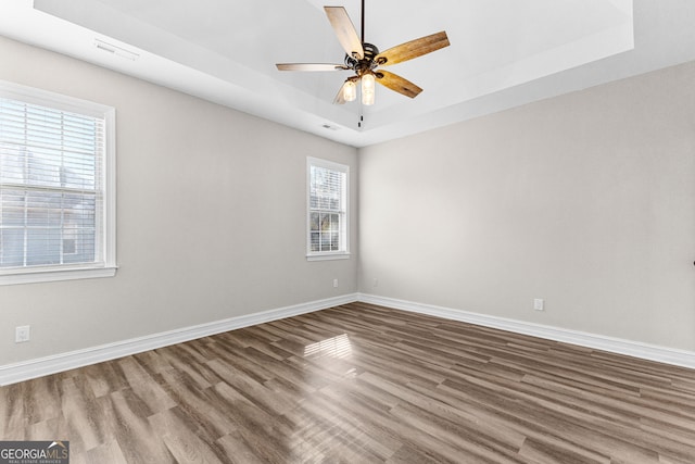 empty room with a raised ceiling, ceiling fan, and hardwood / wood-style floors