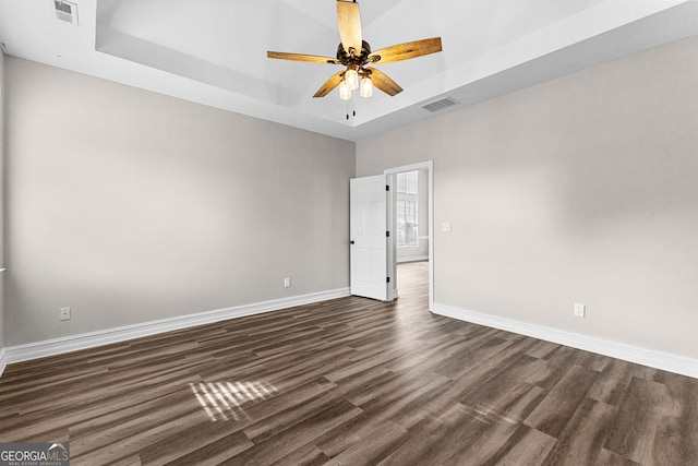 unfurnished room with a tray ceiling, ceiling fan, and dark hardwood / wood-style flooring